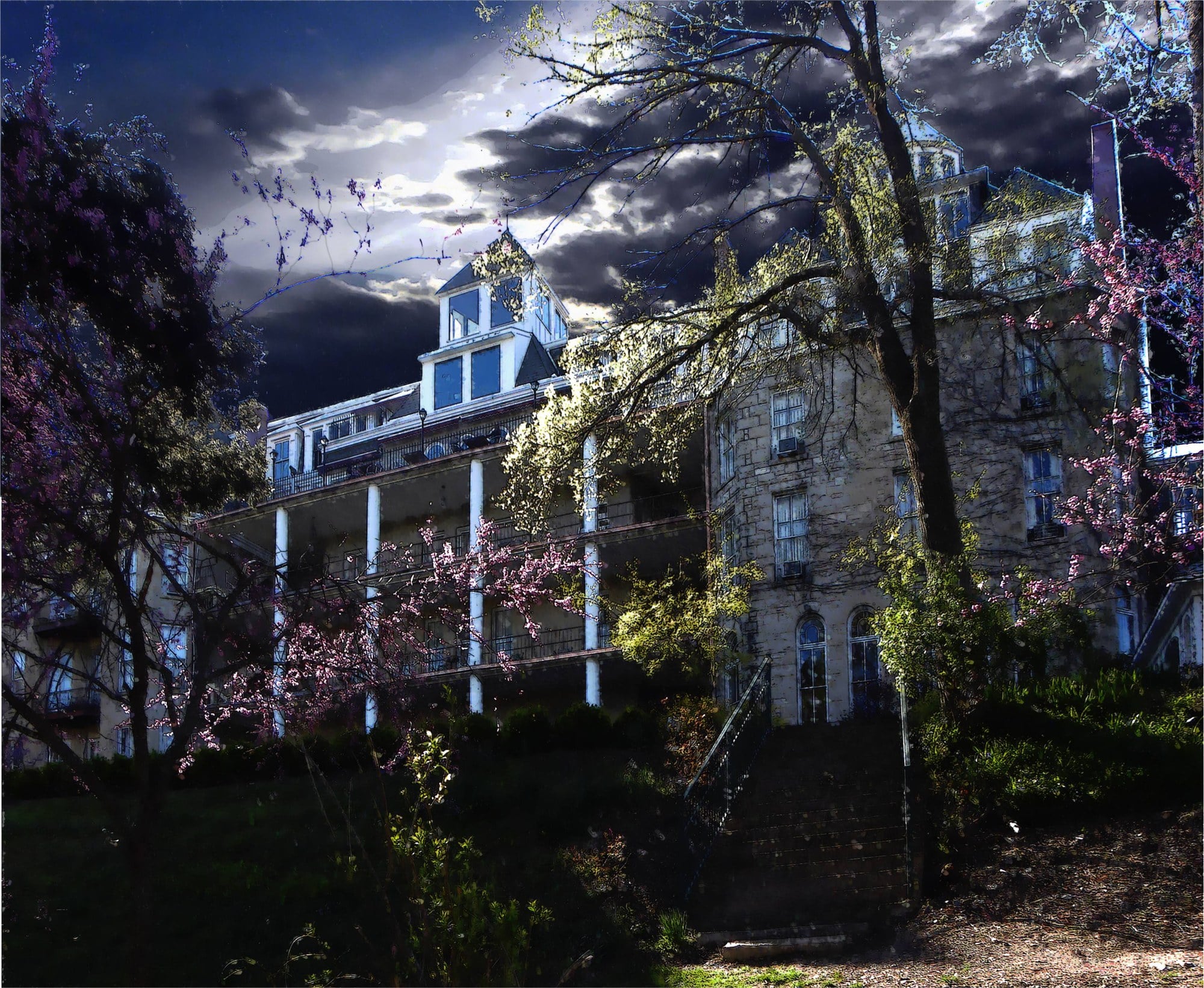 The stone 1886 Crescent Hotel seen through blossoming trees under a dark, stormy sky