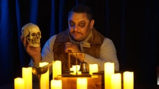 Ambrose T. Attaway holds a skull at the candlelit seance table in Through the Veil
