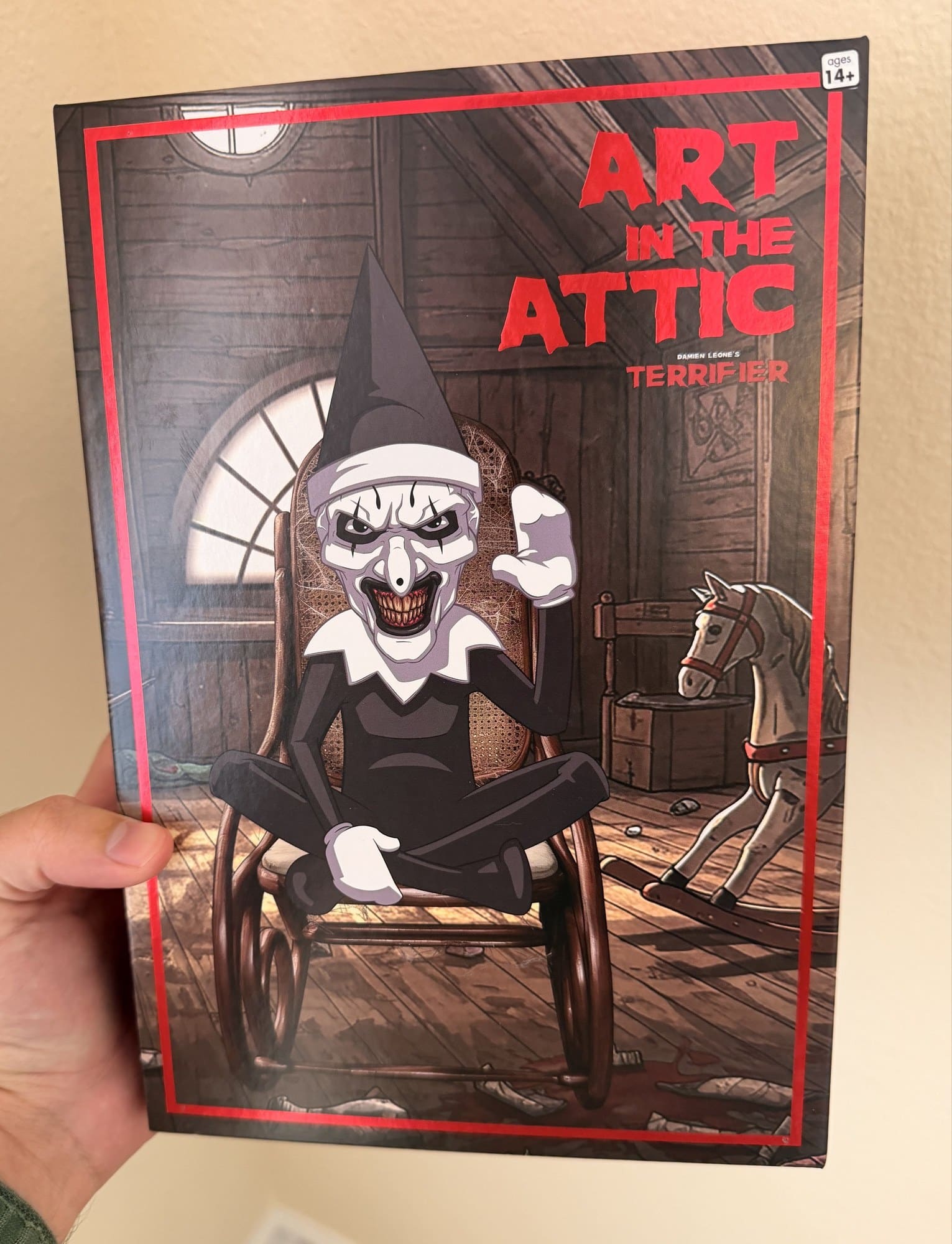 The Art in the Attic box from Damien Leone's Terrifier, showing Art the Clown in an elf hat in a rocking chair in an attic