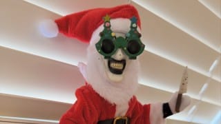 The Art in the Attic doll of Art the Clown in a Santa suit, Santa hat and green Christmas-tree glasses, holding a small knife