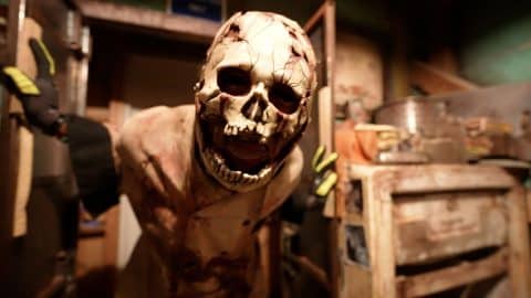 Masked scare actor lunging toward the camera inside a haunted house scene