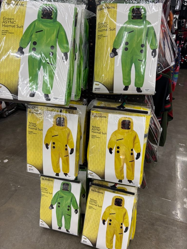 Green and Yellow ASYNC Hazmat Suit costumes in packaging on a Spirit Halloween store shelf