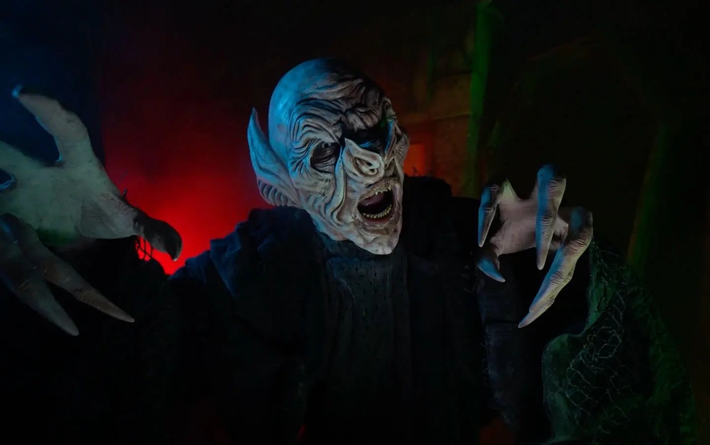 A pale vampire with long clawed fingers leans out of the dark at Bayville Scream Park