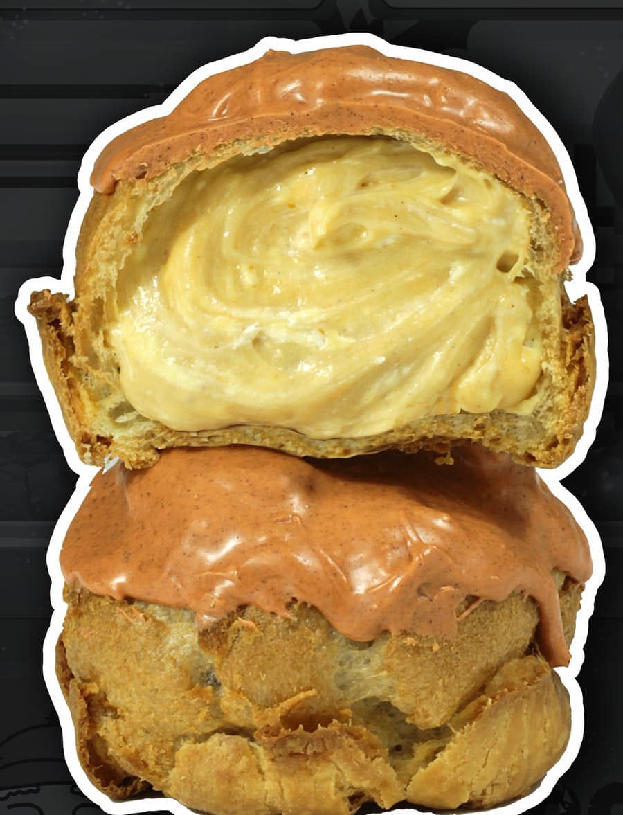 A cream puff cut open to show orange custard, stacked on a whole cream puff with an orange glaze