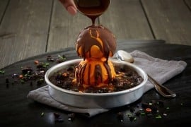 BJ's Spooky Pizookie: a chocolate cookie in a metal pan topped with orange ice cream and a crackable chocolate drizzle, with orange and green Halloween sprinkles.
