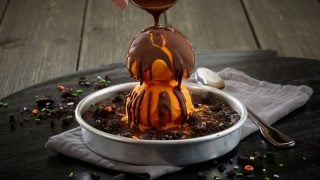 BJ's Spooky Pizookie: a chocolate cookie in a metal pan topped with orange ice cream and a crackable chocolate drizzle, with orange and green Halloween sprinkles.
