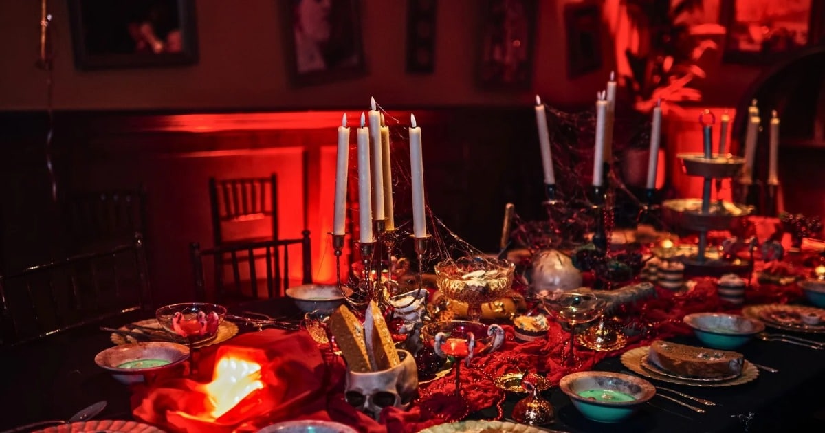 A banquet table set with candles, bowls, and a skull under red light