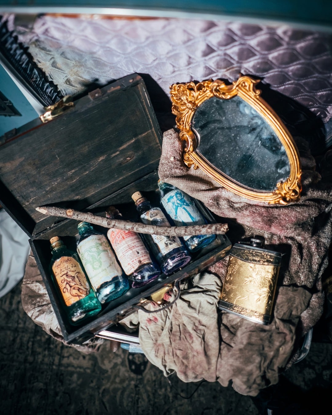 An open wooden case of small glass bottles beside a gilt hand mirror