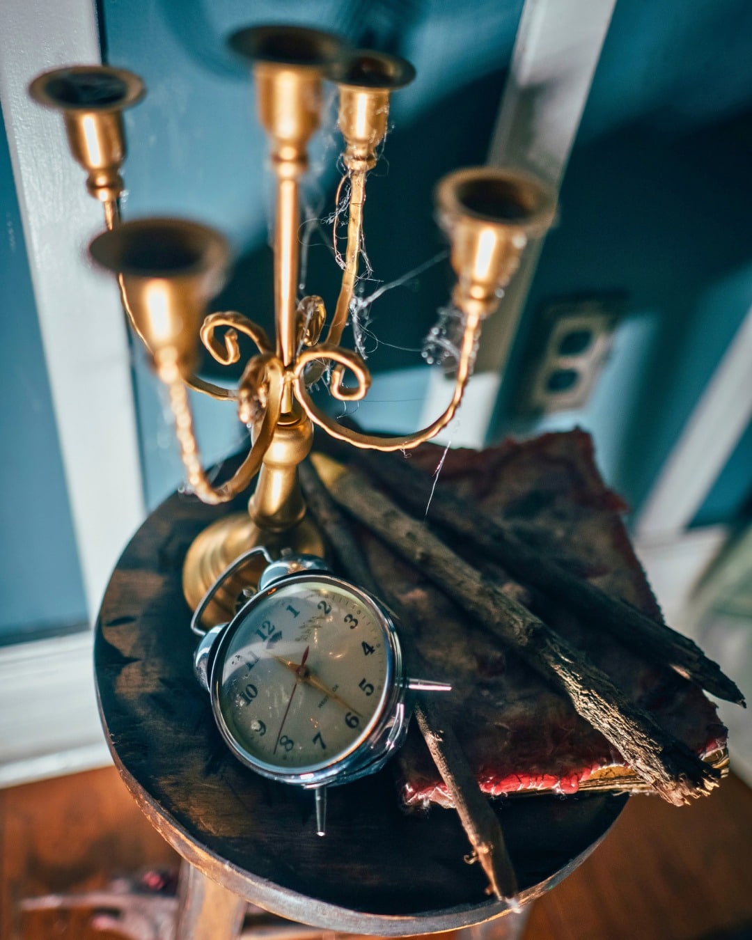 A brass candelabra with cobwebs and an alarm clock on a wooden stool