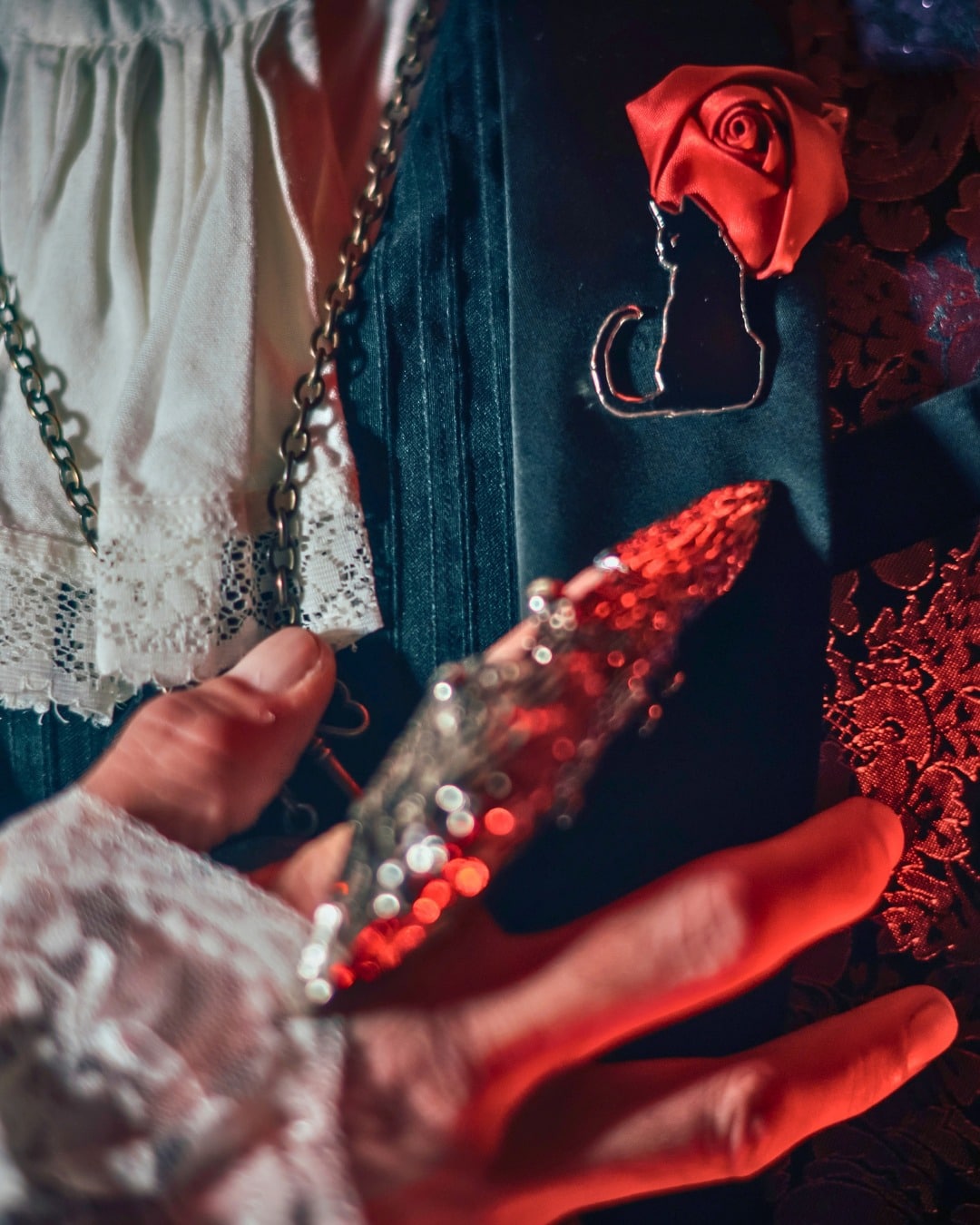 A hand wearing a red sequined claw beside a black cat brooch and a red fabric rose