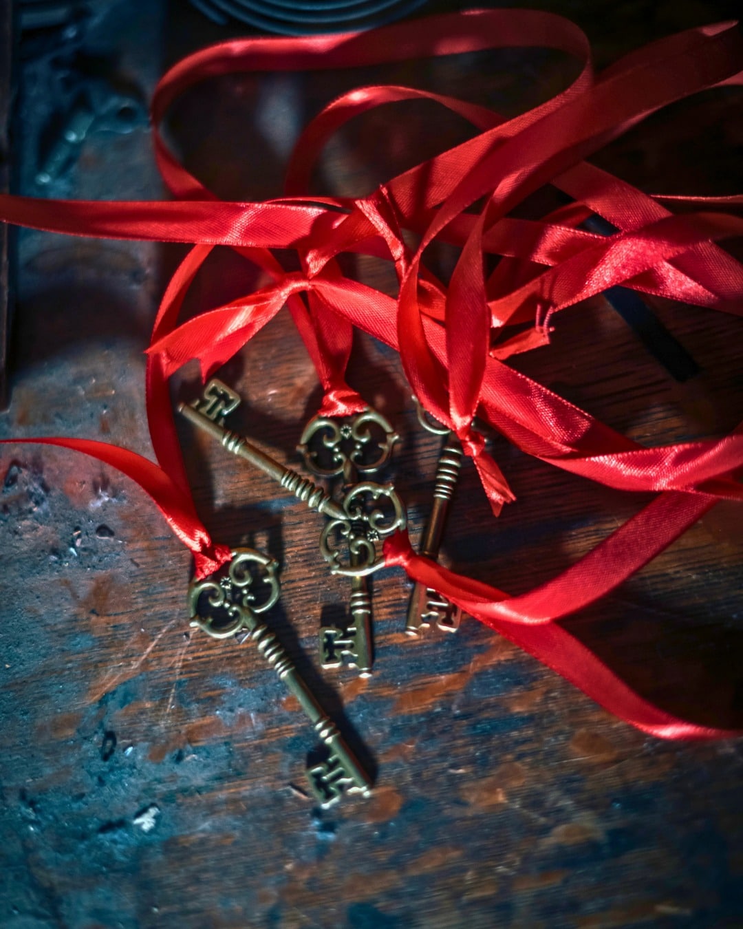 Three brass keys tied to red ribbons on a worn wooden table
