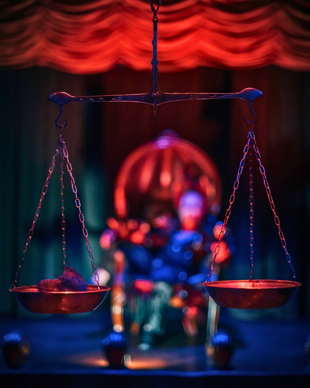 A hanging balance scale in front of a red curtain