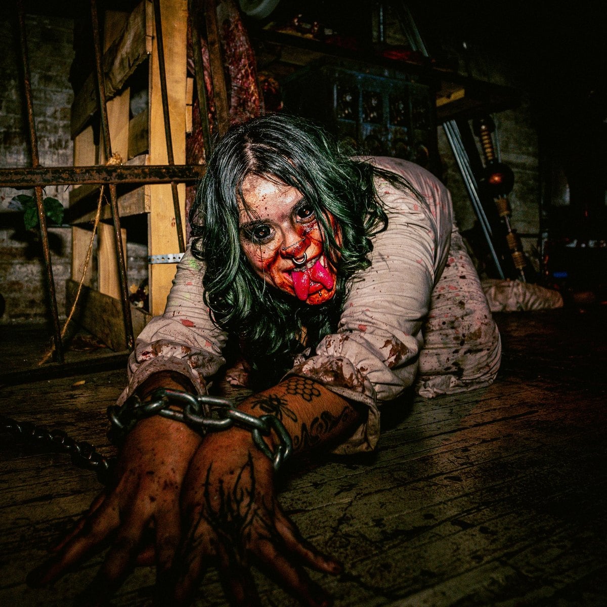 A Blood Manor scare actor with green hair and a bloody mouth crawls across the floor in chains