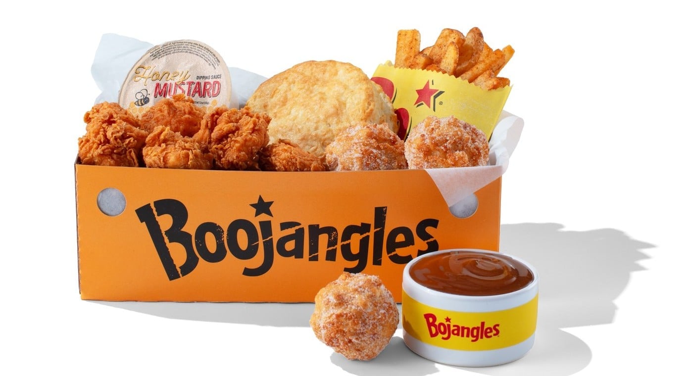 An orange Boojangles box filled with fried chicken bites, a biscuit, fries, a honey mustard cup, and sugar-coated Donut Bites, with a cup of caramel dip beside it
