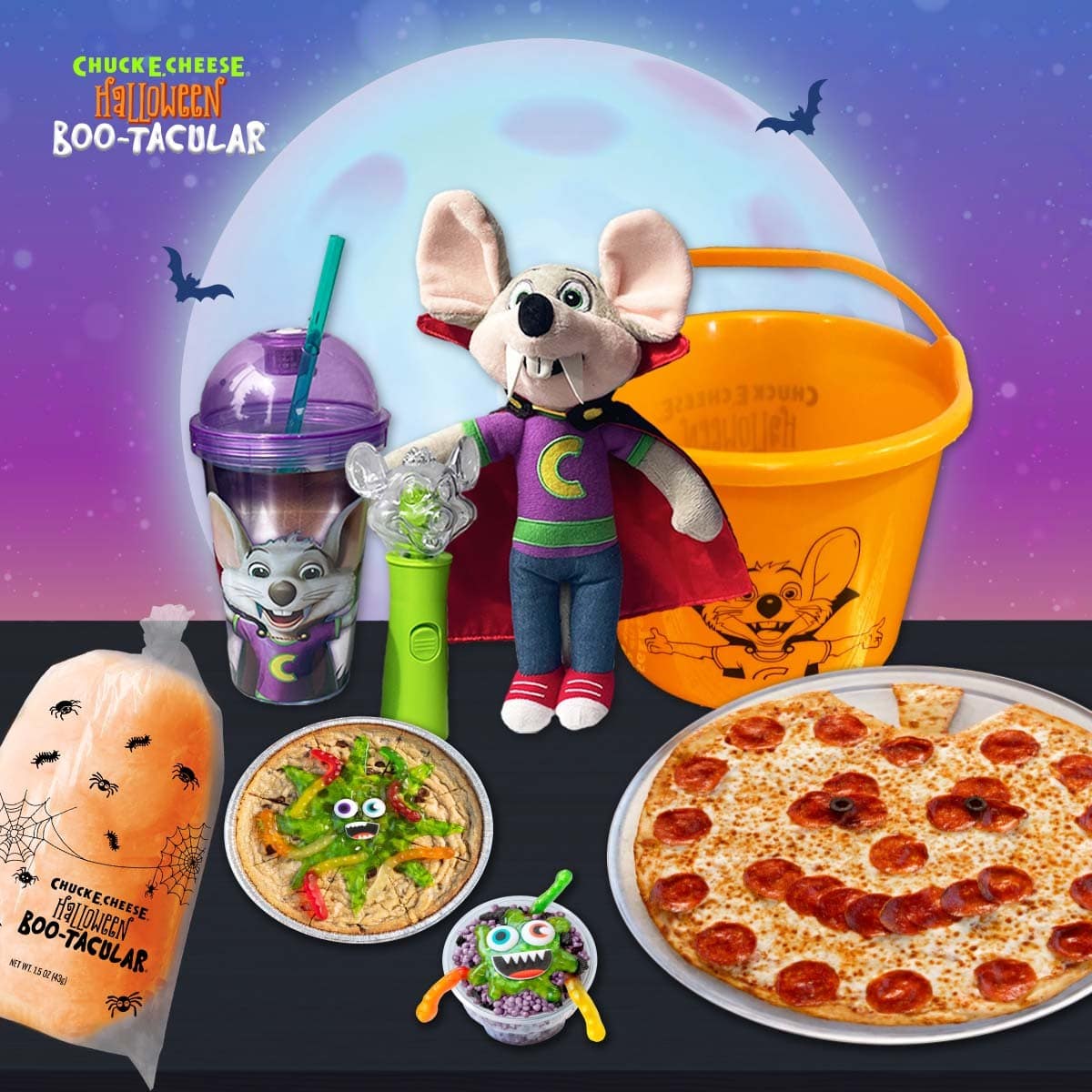 A pumpkin-shaped pepperoni pizza with a plush mouse in a vampire cape, an orange bucket, a purple cup and Halloween treats