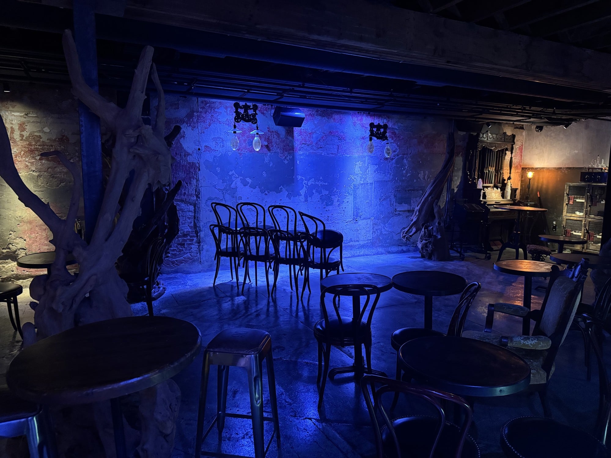 A brick-walled room lit blue with cafe tables, bentwood chairs, and driftwood sculptures