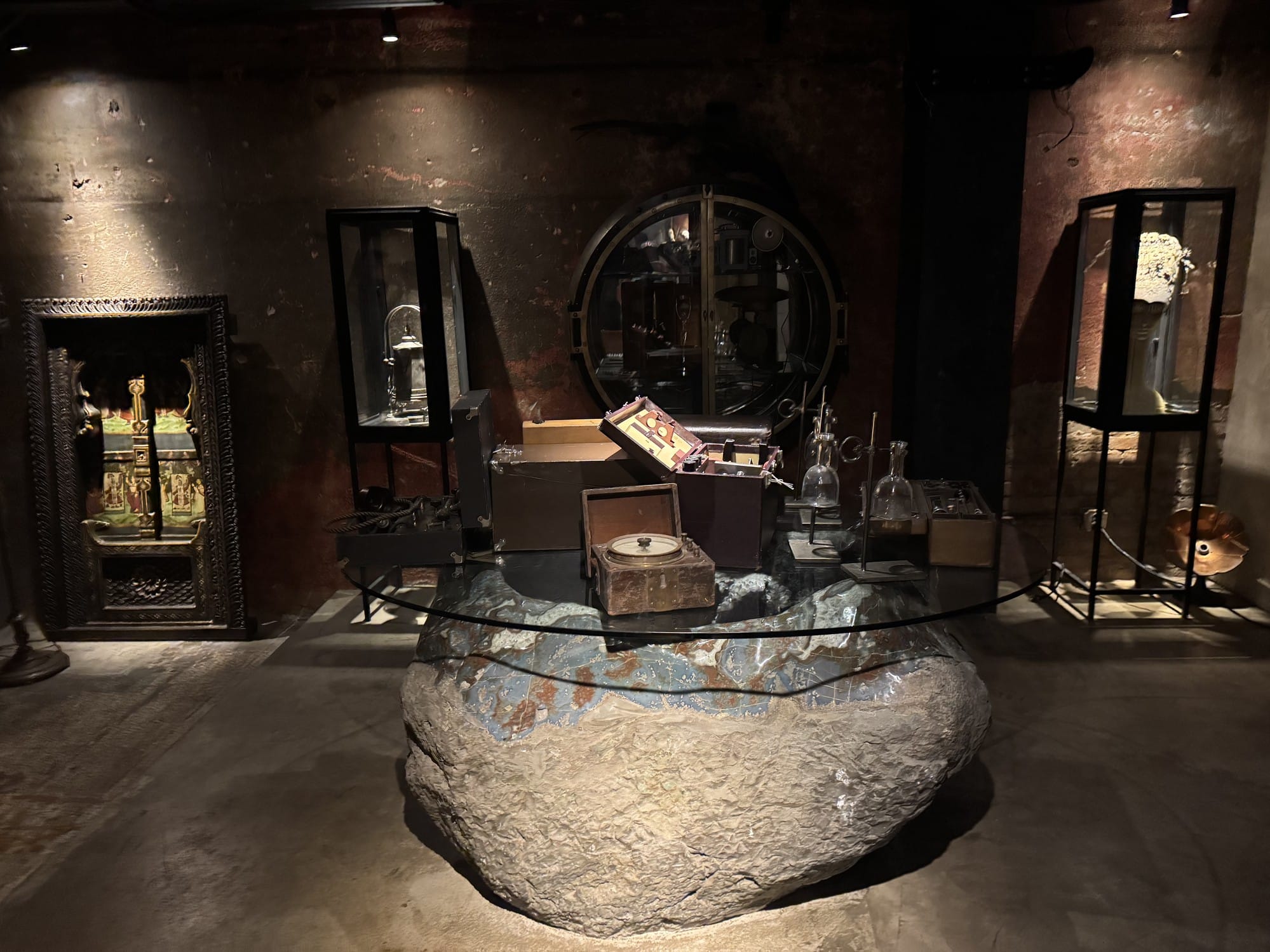 A room with glass display cases, a round vault-style cabinet, and a glass-topped table set on a boulder holding antique instruments
