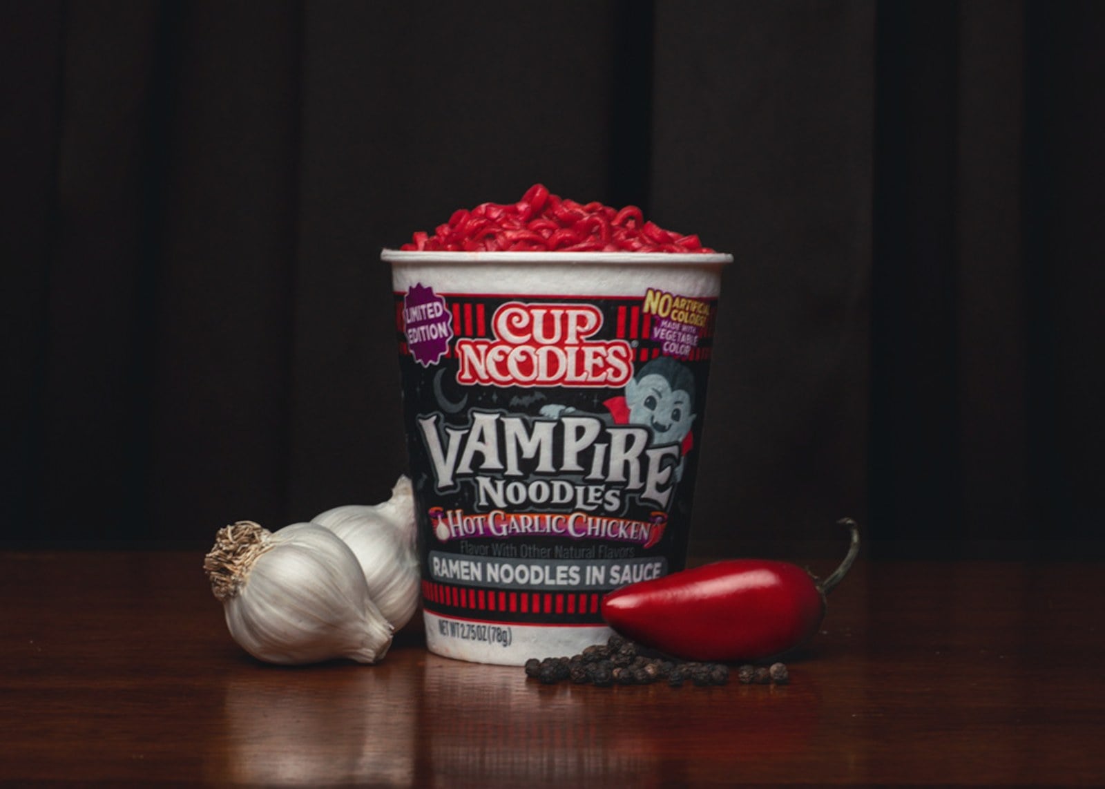 A Cup Noodles Vampire Noodles cup filled with blood-red noodles, beside garlic and a red chili