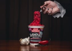 A vampire's hand lifts blood-red Cup Noodles Vampire Noodles from the cup with a fork