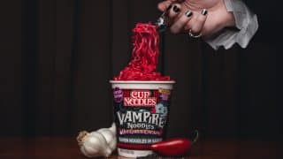 A vampire's hand lifts blood-red Cup Noodles Vampire Noodles from the cup with a fork