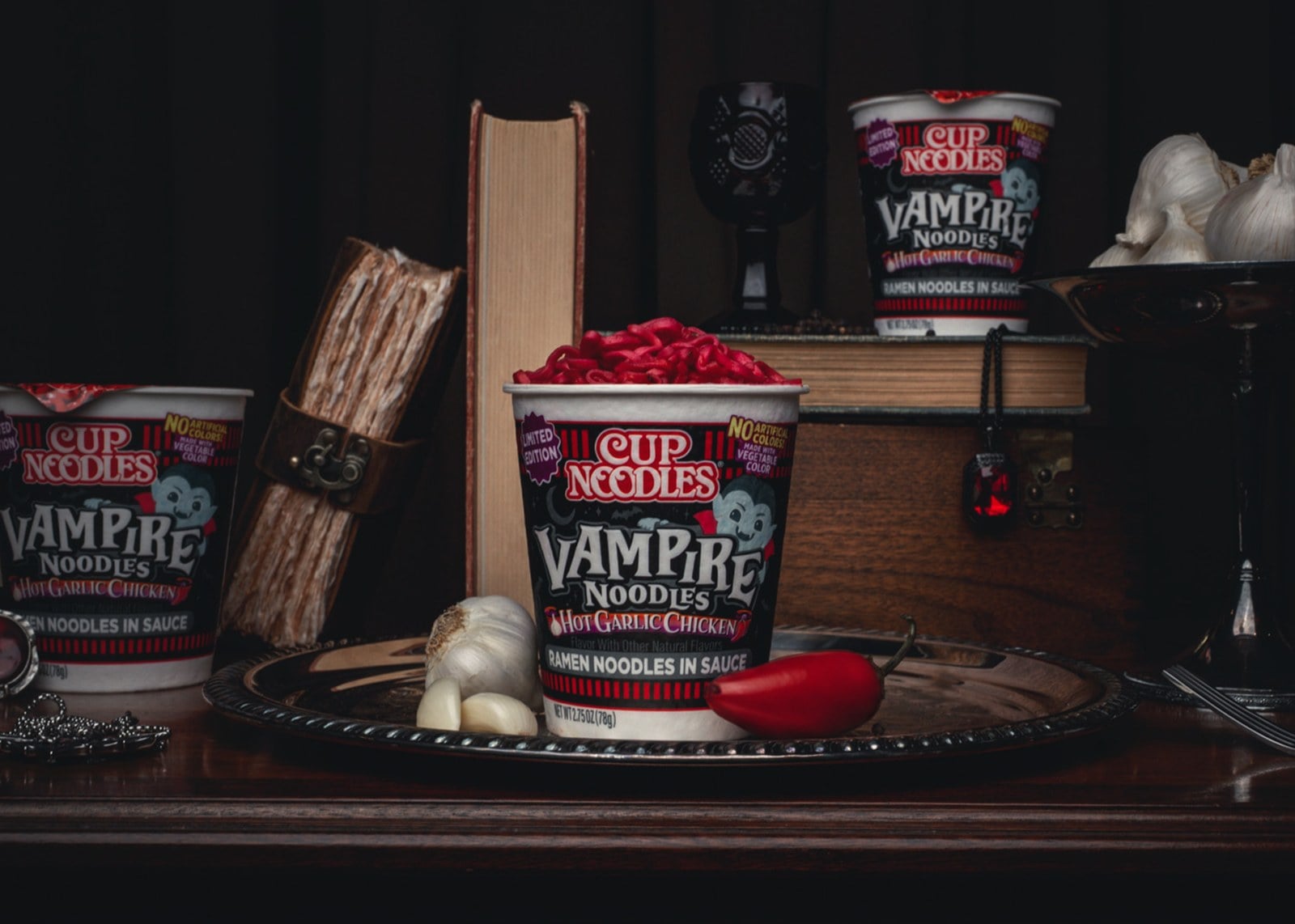 Cup Noodles Vampire Noodles cups on a dark table with old books, a goblet, and garlic