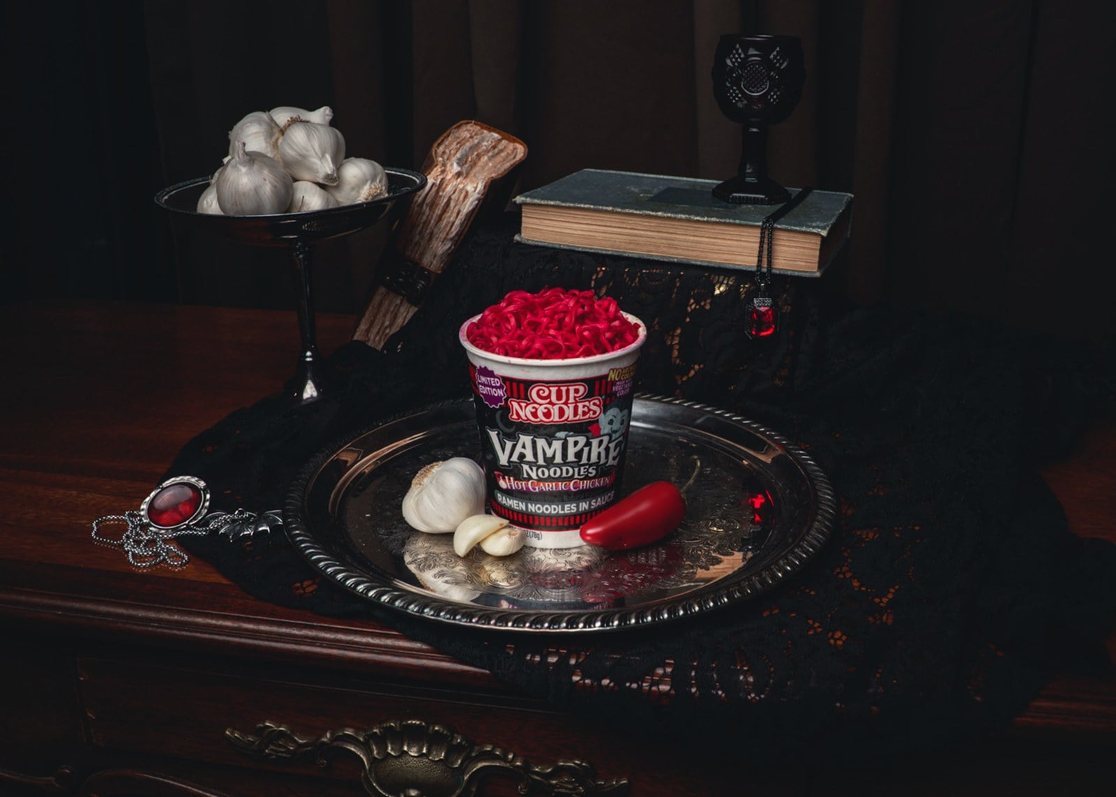 A Cup Noodles Vampire Noodles cup on a silver tray with garlic, a red chili, and a stake