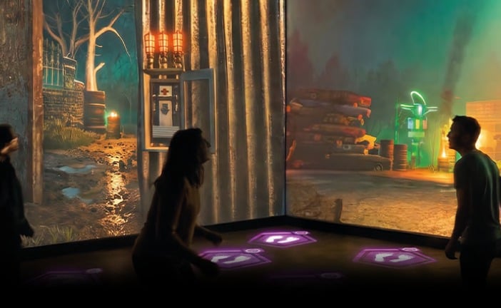 Guests in silhouette stand on glowing purple floor stations in front of projected Dead by Daylight scenery with a lit switch box