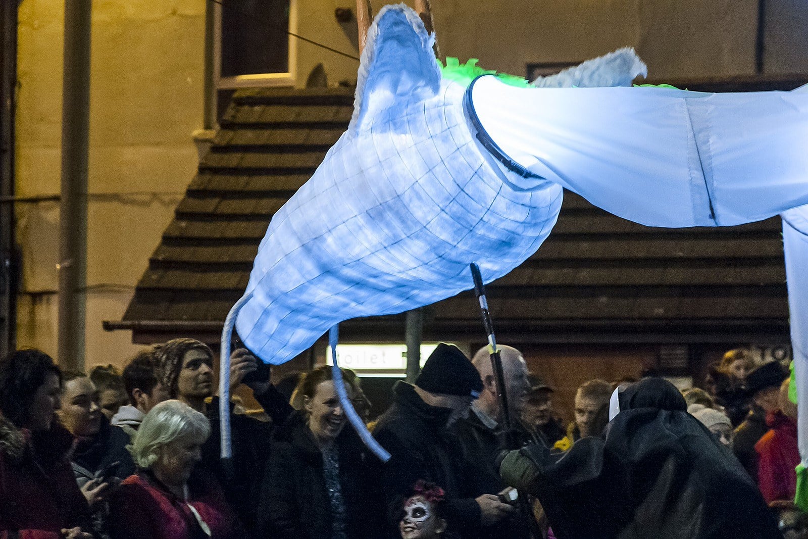 A large white illuminated dragon puppet carried on poles above a crowd at night
