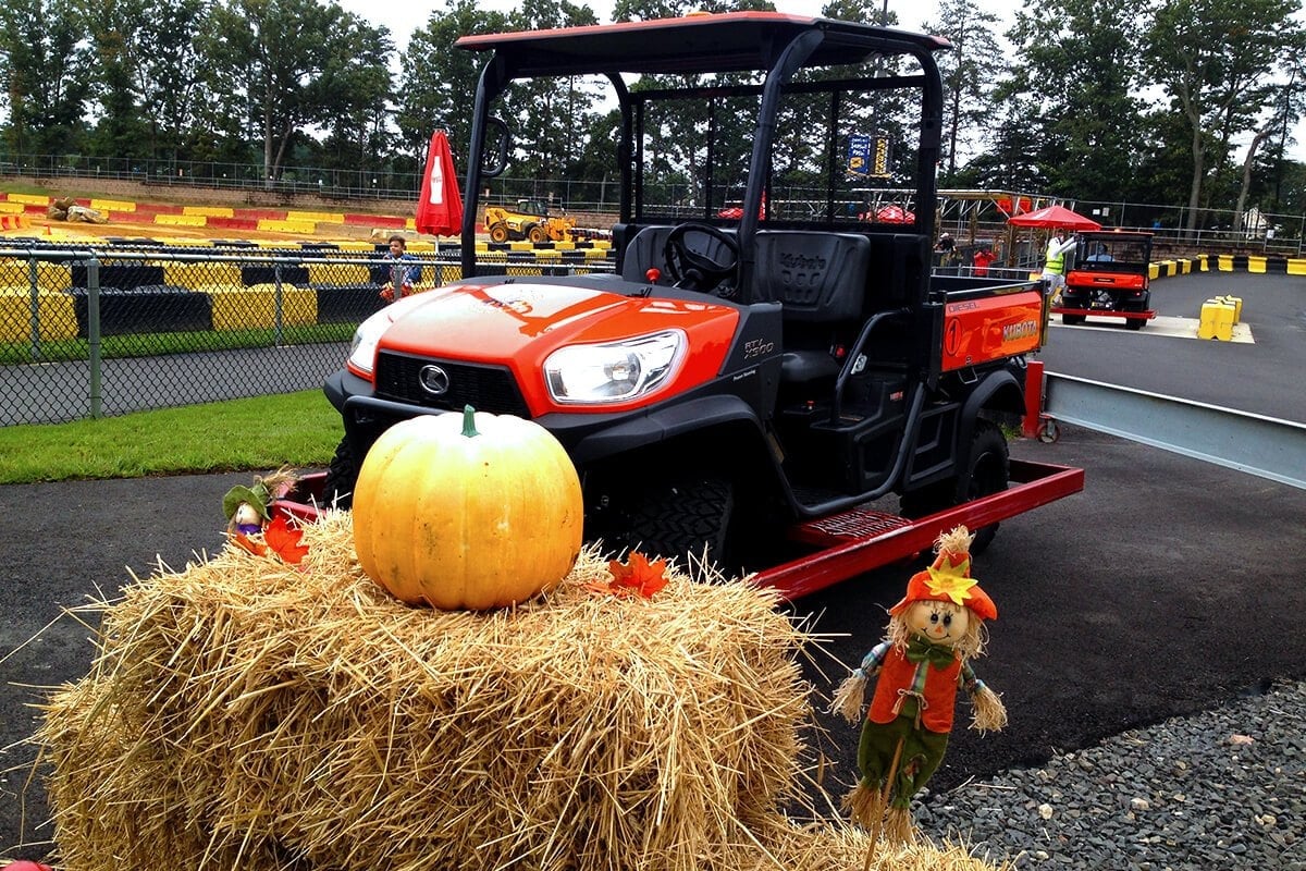 A pumpkin and a scarecrow on a hay bale in front of an orange utility vehicle