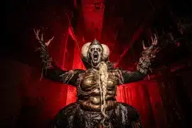 A screaming, horned Blood Prison scare actor in gold body paint stands in a red-lit cell block at the Ohio State Reformatory