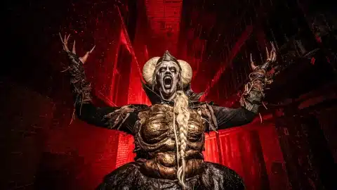A screaming, horned Blood Prison scare actor in gold body paint stands in a red-lit cell block at the Ohio State Reformatory