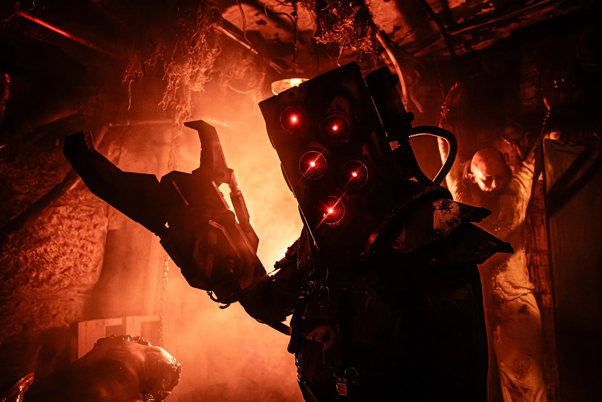 A Blood Prison performer in an apocalyptic mask with glowing red eyes looms in orange smoke inside the haunt