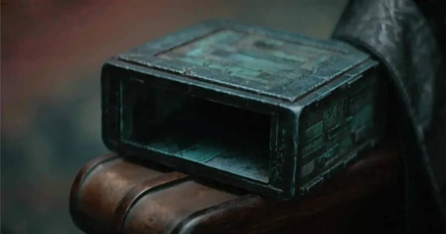 A weathered green metal box with an open side, resting on the arm of a wooden chair