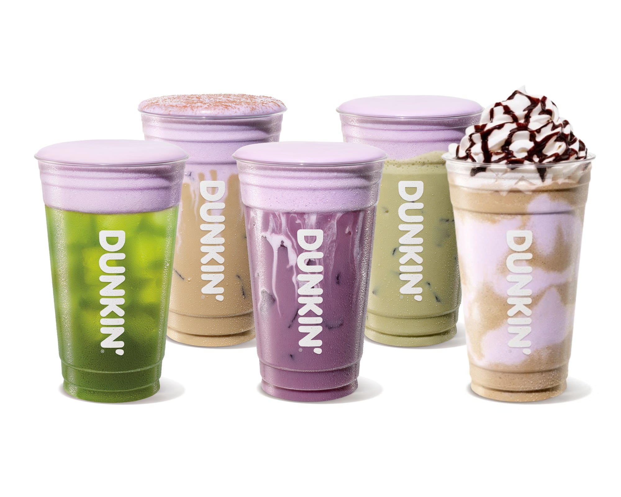 Five iced and frozen Dunkin drinks in clear cups, green, tan, purple, and pale green, topped with purple foam, one with whipped cream and chocolate drizzle