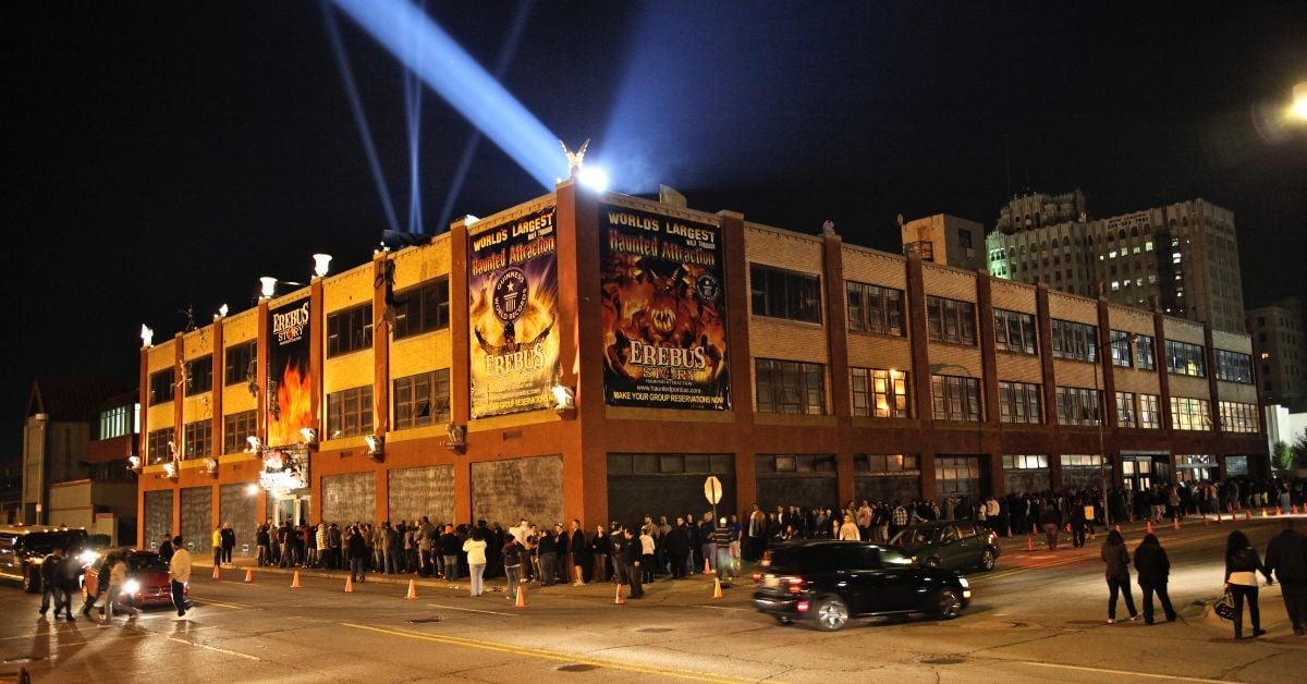 Nighttime crowd lined up outside the four-story Erebus Haunted Attraction building in Pontiac, Michigan, under searchlights