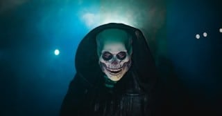 A hooded, skull-faced scareactor in fog at Dorney Park Halloween Haunt