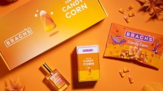 Brach's Ode to Candy Corn eau de parfum box and bottle with a bag of Brach's Classic Candy Corn and fall leaves on an orange background