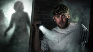 A Fright Nights guest holds a failing torch as a figure looms in the dark inside Thorpe Park's Tenement maze
