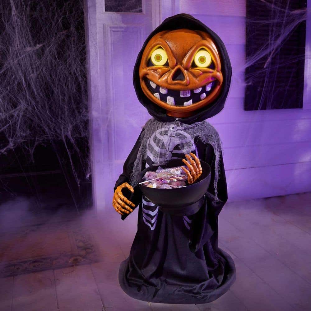 Gemmy 3 ft Animated Pumpkin Skeleton with Candy Bowl at Home Depot: a black-cloaked skeleton with a grinning jack-o'-lantern head and glowing eyes, one hand on a candy bowl, in a cobwebbed room