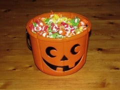 An orange jack-o'-lantern candy bucket filled with wrapped candy on a wooden table