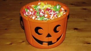 An orange jack-o'-lantern candy bucket filled with wrapped candy on a wooden table