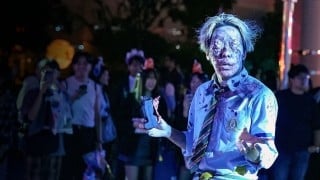 A street zombie performer in a blood-spattered school uniform at Universal Studios Japan, with guests filming behind him