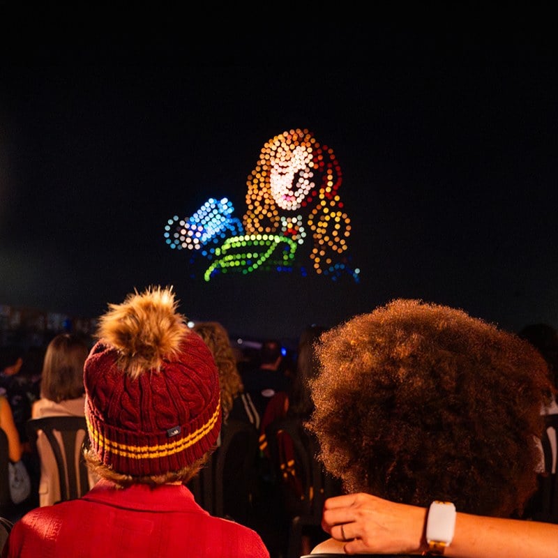 Drones form a glowing portrait of Hermione Granger above a crowd in Harry Potter scarves and hats