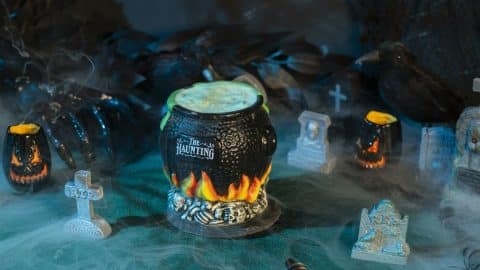 A cauldron-shaped The Haunting cocktail mug with a green drink, set among tombstones and fog