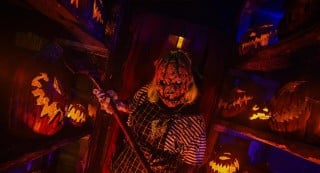 A pumpkin-headed scareactor holding a scythe among carved jack-o'-lanterns at Frightworld in Buffalo.