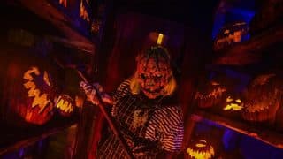 A pumpkin-headed scareactor holding a scythe among carved jack-o'-lanterns at Frightworld in Buffalo.