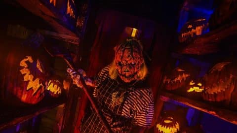 A pumpkin-headed scareactor holding a scythe among carved jack-o'-lanterns at Frightworld in Buffalo.