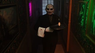 A masked butler in a tuxedo holding a silver tray and a bloodied napkin in a long, dim hallway of the Estate of Evil