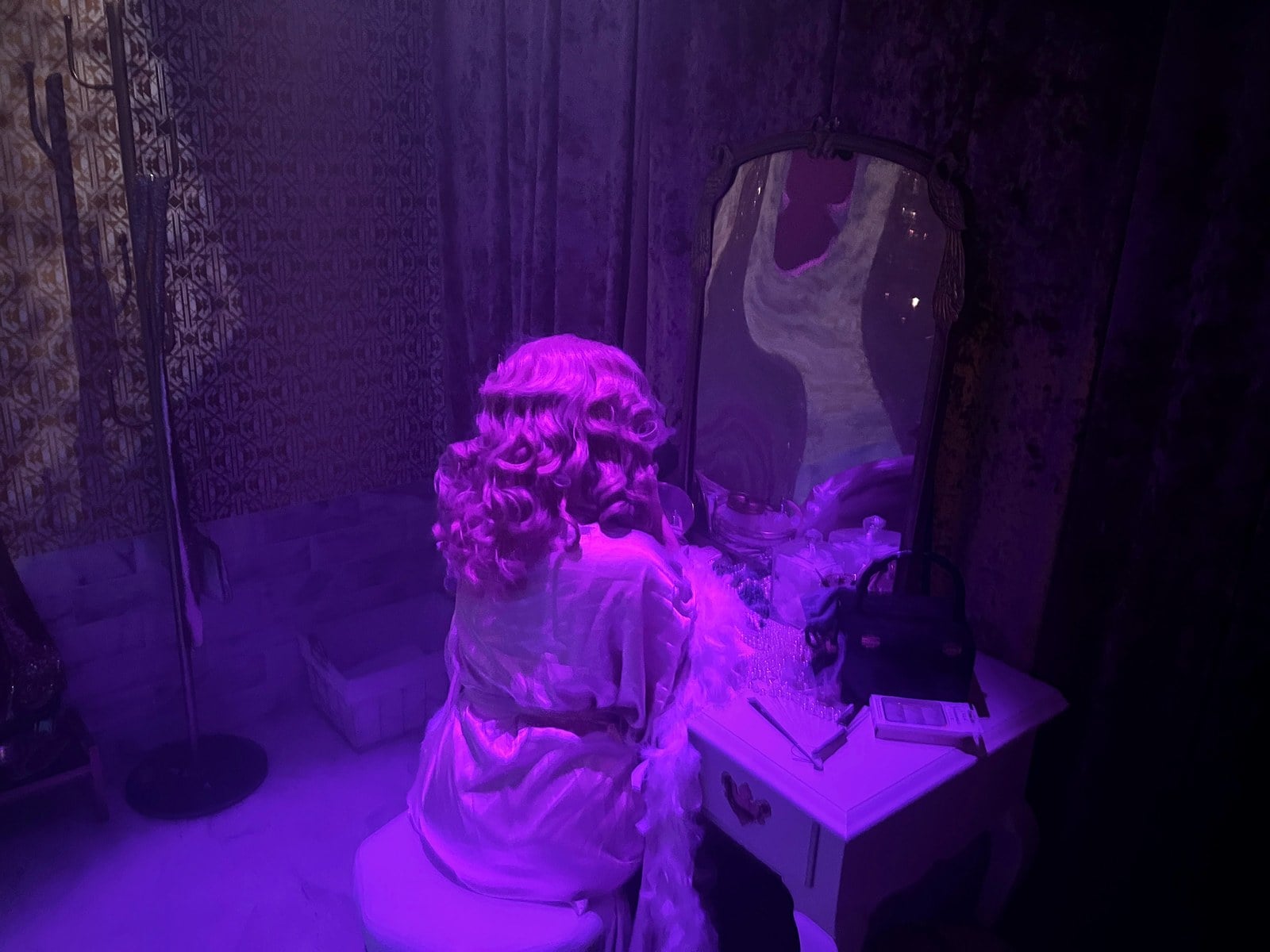 A 1950s starlet figure at a vanity mirror under purple light in the Estate of Evil's envy room