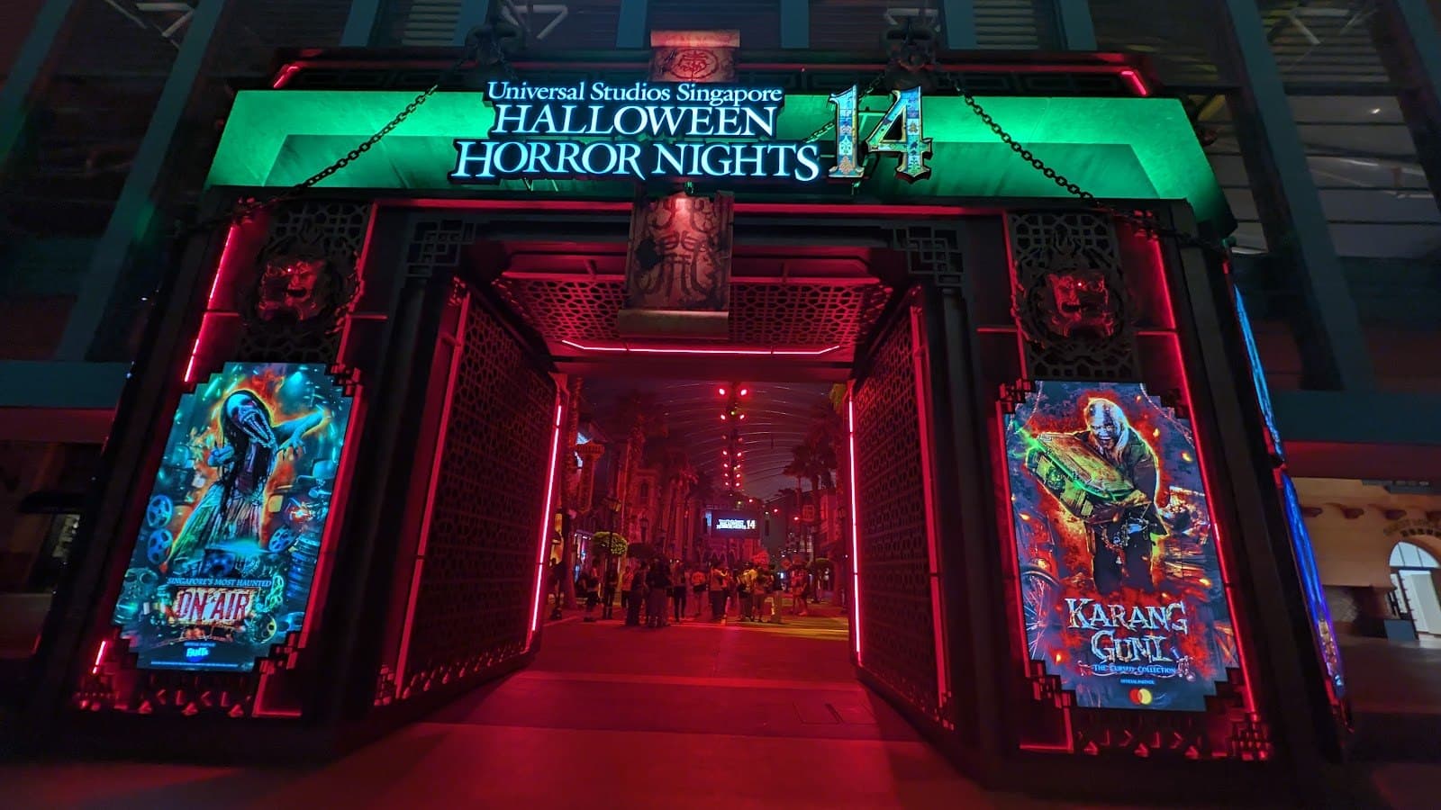 A red and green lit gateway with a Halloween Horror Nights 14 sign and tall illustrated panels on each side, at night